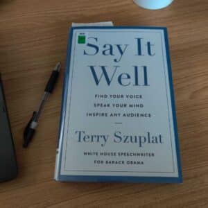 A book laying on a desk with a pen nearby. The title is Say It Well by Terry Szuplat.